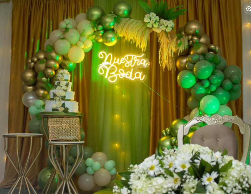 Montaje de boda con arco de globos verdes y dorados y torta de tres pisos