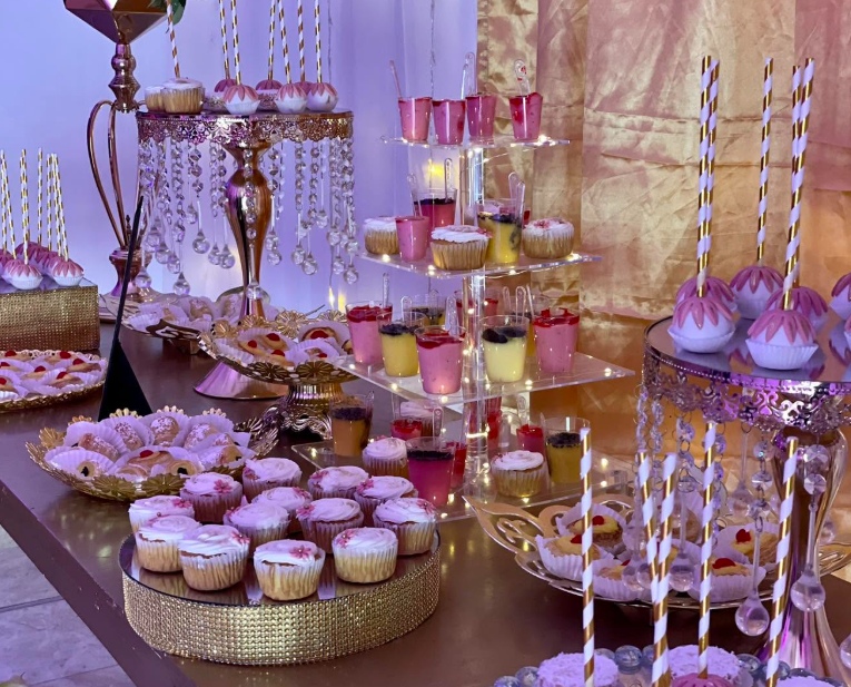 Mesa de postres iluminada con cupcakes, gelatinas y bases doradas con cristales